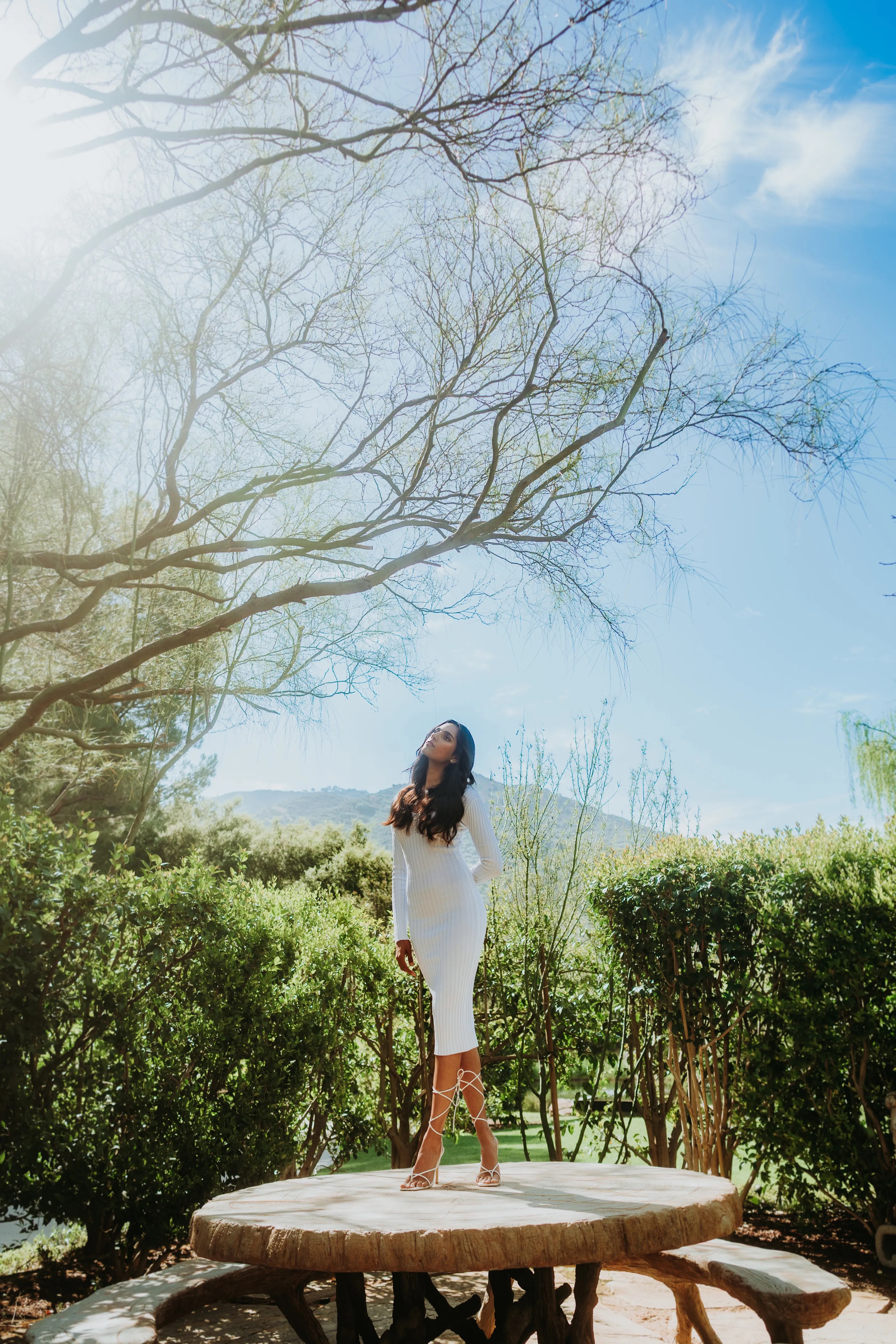 Diya Patel standing on a table in a white dress looking up at the sunlight